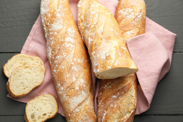 Cut fresh baguettes on grey wooden table, top view