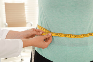 Nutritionist measuring overweight woman's waist with tape in hospital, closeup