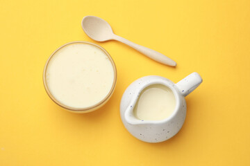 Tasty condensed milk in bowl and jug with spoon on orange background, top view