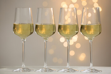 Tasty white wine in glasses on table against grey background with blurred lights, bokeh effect
