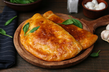 Tasty calzones with basil and mozzarella cheese on wooden table, closeup