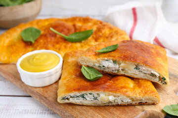 Tasty calzones with basil, cheese and sauce on white wooden table, closeup