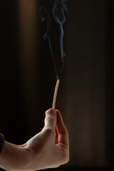 A hand holds a long match that is extinguished and smoking