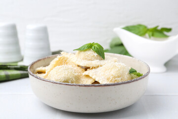 Delicious ravioli with cheese and basil on white tiled table, closeup