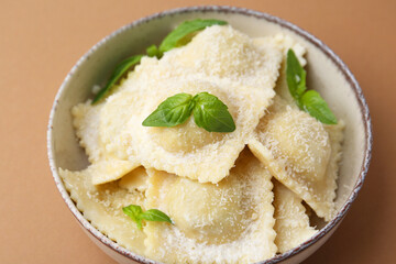 Delicious ravioli with cheese and basil on brown background, closeup