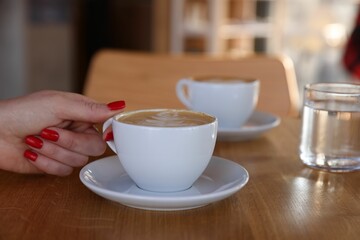 Woman with cup of aromatic coffee at wooden table in cafe, closeup