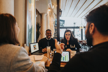 Diverse people collaborating during a meeting in a stylish cafe environment. They are discussing charts and data displayed on laptops and tablets, highlighting teamwork, productivity, and creativity.