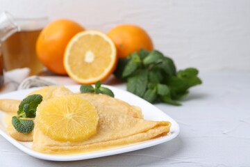 Delicious Crepes Suzette, mint and oranges on white textured table, closeup