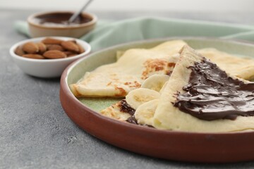 Delicious crepes with chocolate sauce and banana on grey table, closeup