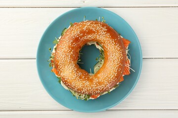 Delicious bagel with salmon, microgreens and cucumber on white wooden table, top view