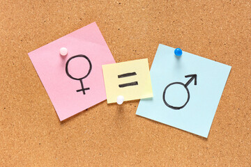 Stickers with equal sign, female and male gender symbols on cork board as background