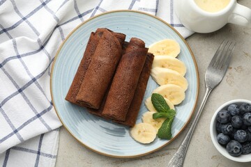 Delicious chocolate crepes with banana and blueberries served on light table, flat lay