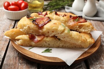 Slices of delicious focaccia bread with bacon, rosemary and tomatoes on wooden table, closeup