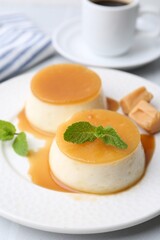Tasty puddings with caramel sauce served on white tiled table, closeup