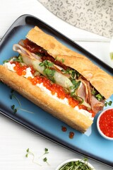 Delicious baguette sandwich with caviar, ham and capers on white wooden table, top view