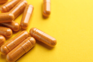 Turmeric capsules on yellow background, closeup. Space for text