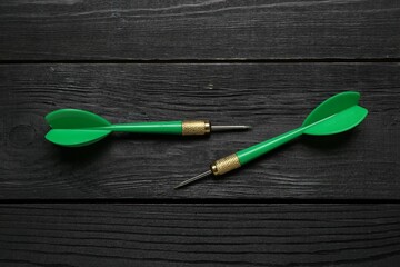 Green dart arrows on black wooden table, flat lay