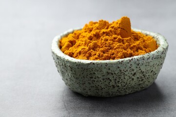 Turmeric powder in bowl on grey table, closeup