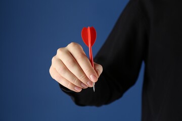 Woman holding dart on blue background, closeup