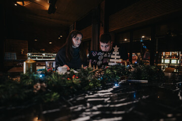 Two individuals are focused on their computer in a warmly decorated caf&eacute;, enhanced with Christmas ornaments that create a peaceful and festive atmosphere. This image represents teamwork, celebration