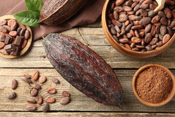 Cocoa pod, powder and beans on wooden table, flat lay