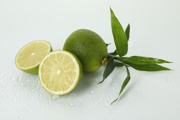 Fresh limes and bamboo leaves on wet surface against white background