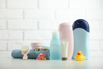 Baby cosmetic products, pacifier, towel and rubber duck on table against white brick wall
