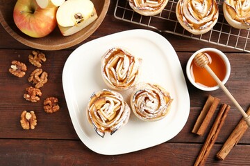 Tasty apple roses with powdered sugar served on wooden table, flat lay