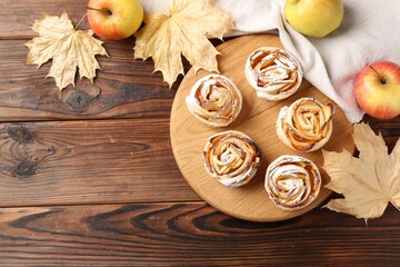Freshly baked apple roses, fruits and dry leaves on wooden table, flat lay. Space for text