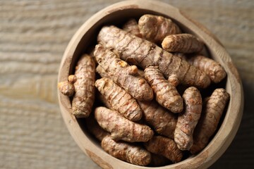 Raw turmeric roots in bowl on wooden table, closeup