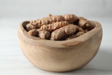 Raw turmeric roots in bowl on white marble table, closeup