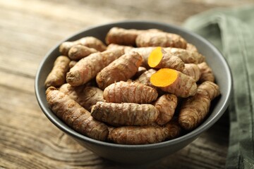 Tumeric rhizomes in bowl on wooden table, closeup
