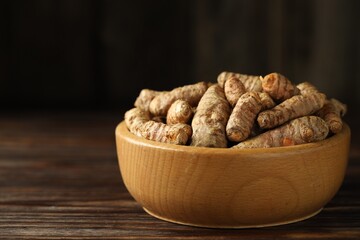 Tumeric rhizomes in bowl on wooden table, closeup