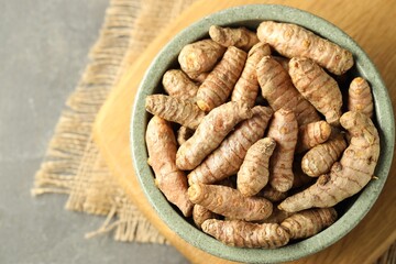 Tumeric rhizomes in bowl on grey table, top view