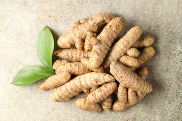 Pile of tumeric rhizomes with leaves on grey table, top view