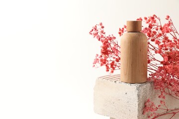 Bottle of cosmetic product and pink gypsophila flowers on concrete block against white background,...
