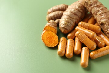 Turmeric rhizomes and capsules on green background, closeup. Space for text