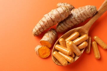 Turmeric rhizomes, capsules and spoon on orange background, flat lay. Space for text