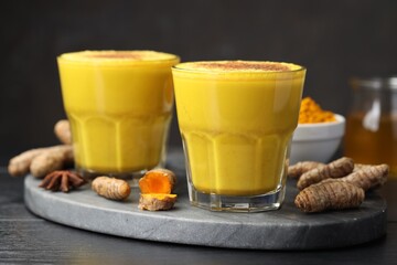 Delicious turmeric latte, powder and rhizomes on black wooden table, closeup
