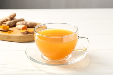 Aromatic turmeric tea in glass cup, roots and powder on white wooden table, closeup