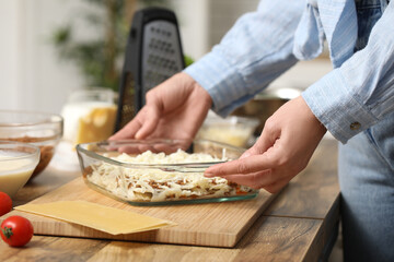 Beautiful mature woman holding baking dish with raw delicious lasagna in kitchen, closeup