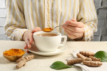 Woman making turmeric tea at white textured table, closeup