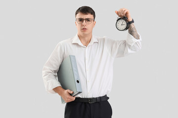 Worried male office worker with alarm clock on light background