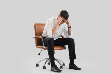 Worried male office worker sitting on chair against light background