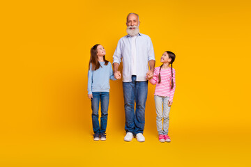Grandfather bonding with two happy granddaughters on a yellow background celebrating their day together