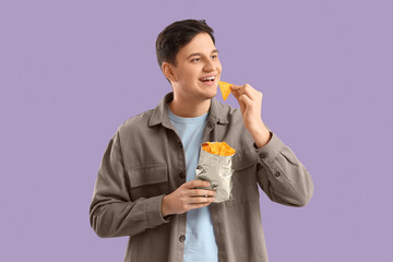 Fototapeta premium Young man eating tasty nachos on lilac background