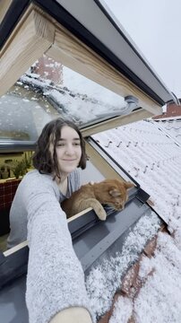 Woman and cat enjoy snowy view from window roof