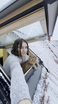 Woman with cat enjoys snowy view from roof window