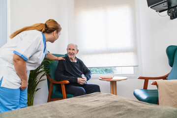 Nurse comforting elderly man sitting in nursing home room
