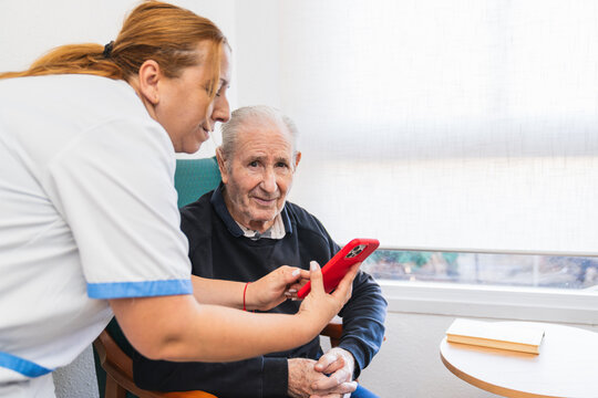 Nurse assisting elderly man with smartphone in nursing home